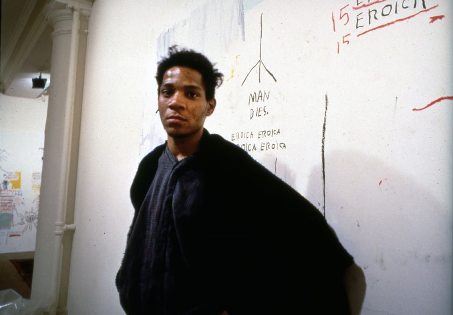 portrait of contemporary artist Jean-Michel Basquiat, “MAN DIES” scribbled on painting behind him
